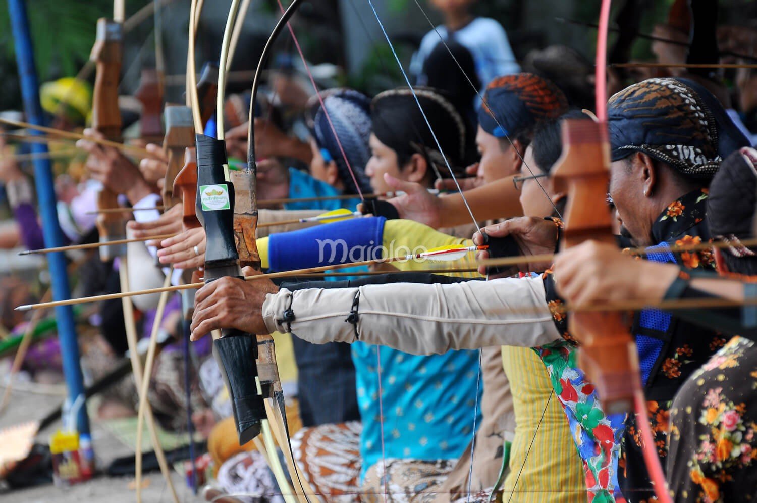 Row of archers taking aim with bows during a Jemparingan competition.