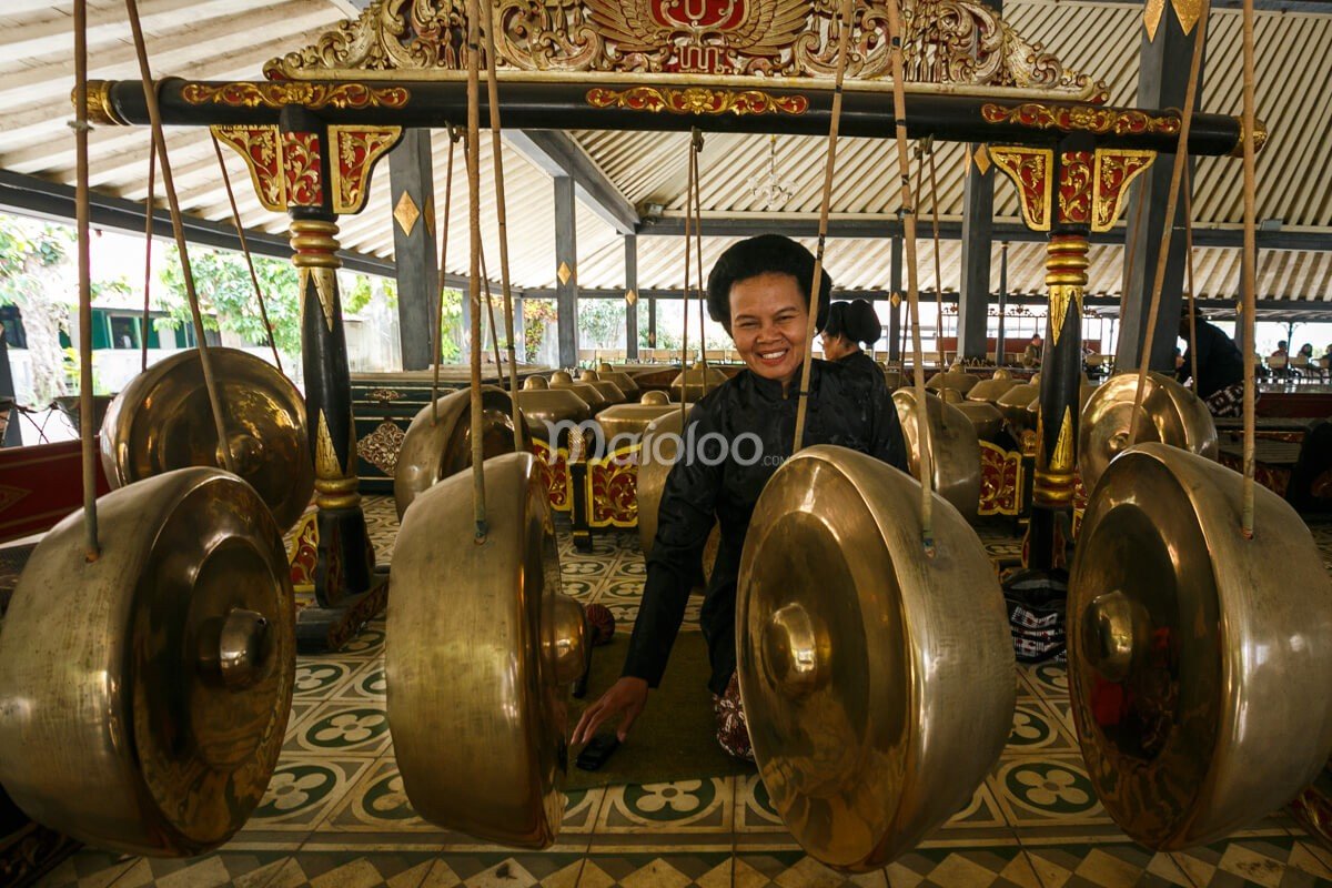 A musician smiling while playing traditional gamelan instruments at Bangsal Sri Manganti in Yogyakarta Palace.