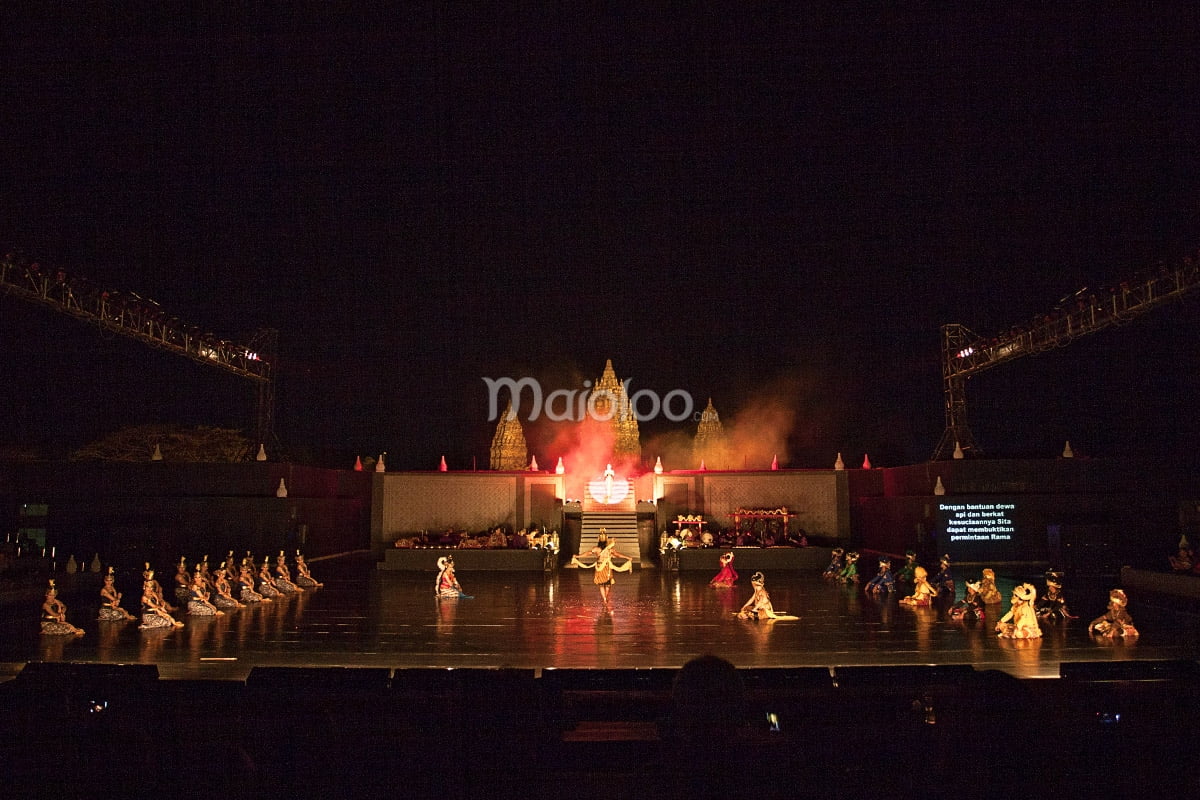 Performers on a large open stage during the Ramayana Ballet with Prambanan Temple illuminated in the background at night.