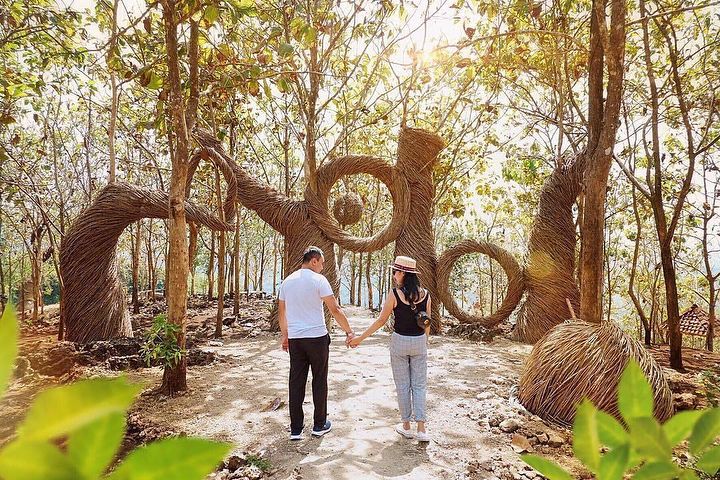 A couple holds hands while walking along a forest path, with intricate natural wicker installations at Geoforest Watu Payung Turunan.