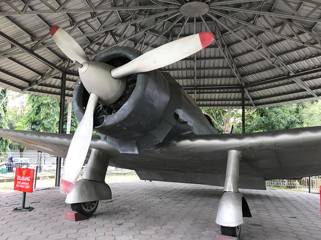 A propeller airplane displayed under a shelter at Monumen Jogja Kembali.