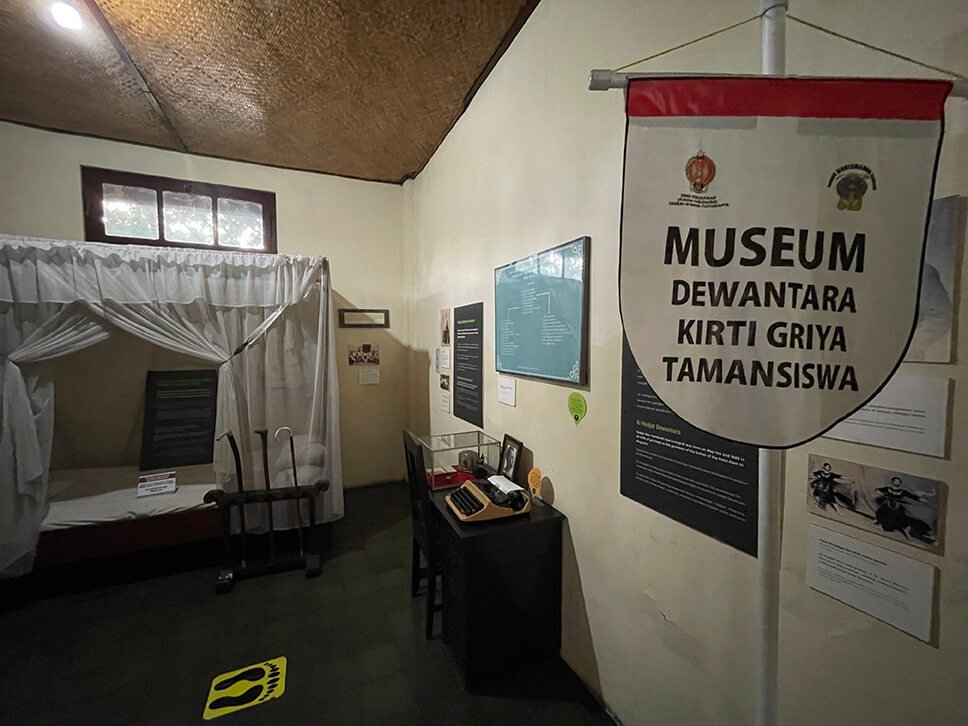 Exhibit showing a bed, typewriter, and informational displays in Dewantara Kirti Griya Museum.