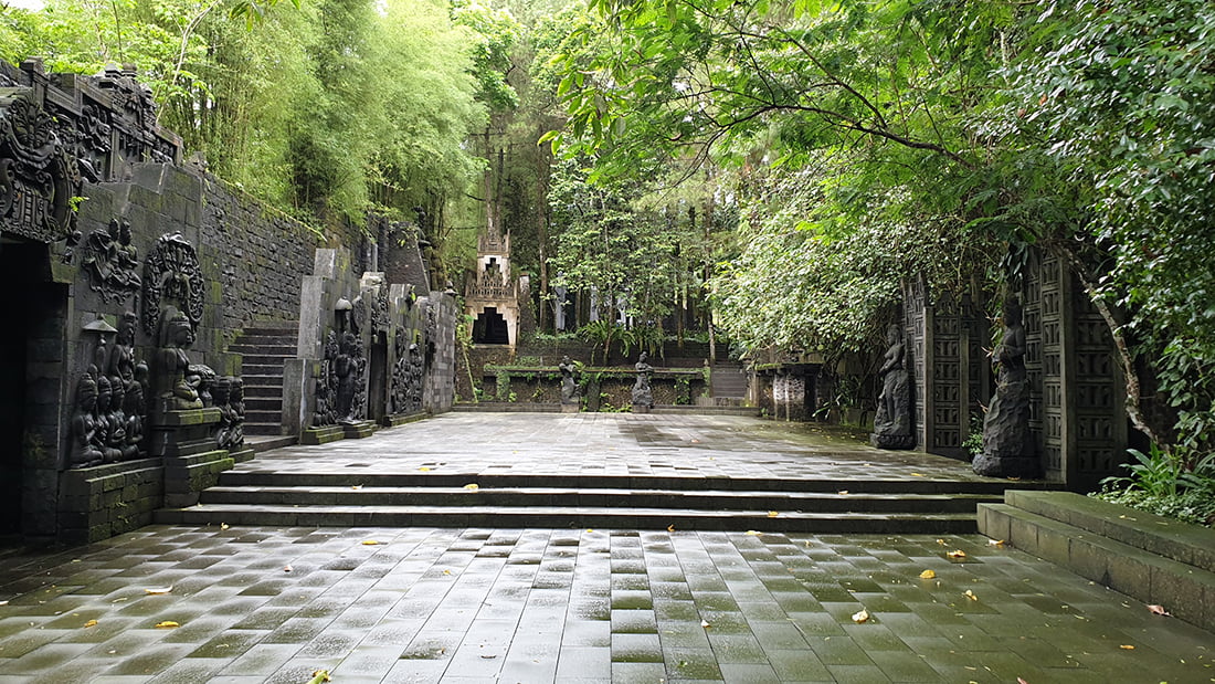 Stone courtyard with intricate carvings and green foliage at Ullen Sentalu Museum.