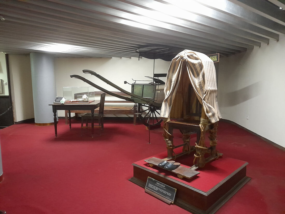 Exhibit of historical furniture and a traditional palanquin at Monumen Jogja Kembali.