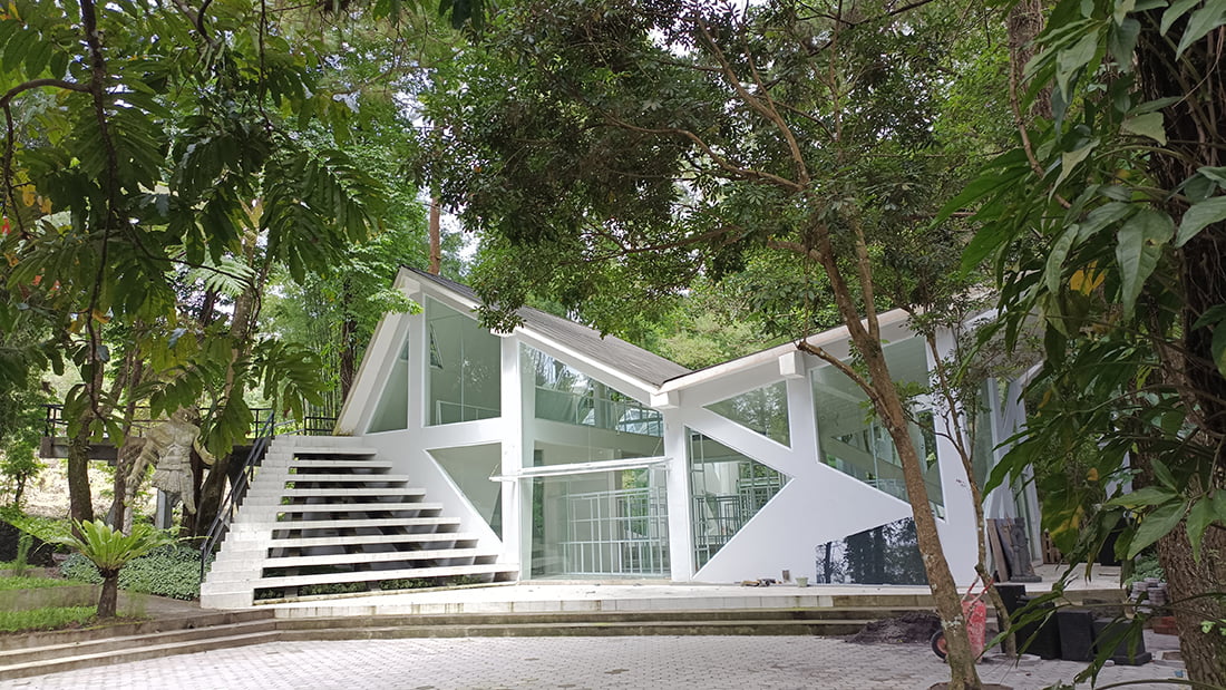 A modern white building with glass walls surrounded by trees at Ullen Sentalu Museum.