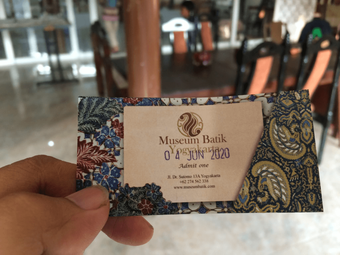 A hand holding a ticket for Museum Batik Yogyakarta with intricate batik patterns.