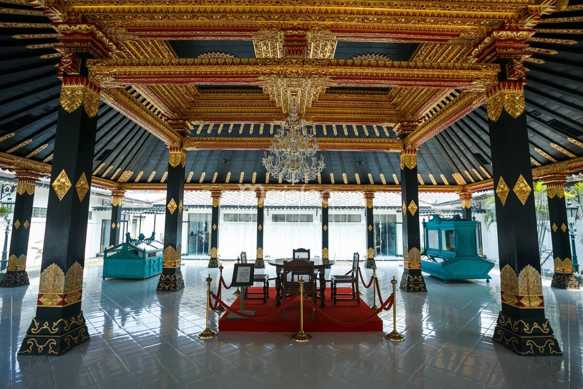 The interior of a room in Yogyakarta Palace with golden decorations, chandeliers, and traditional furnishings.