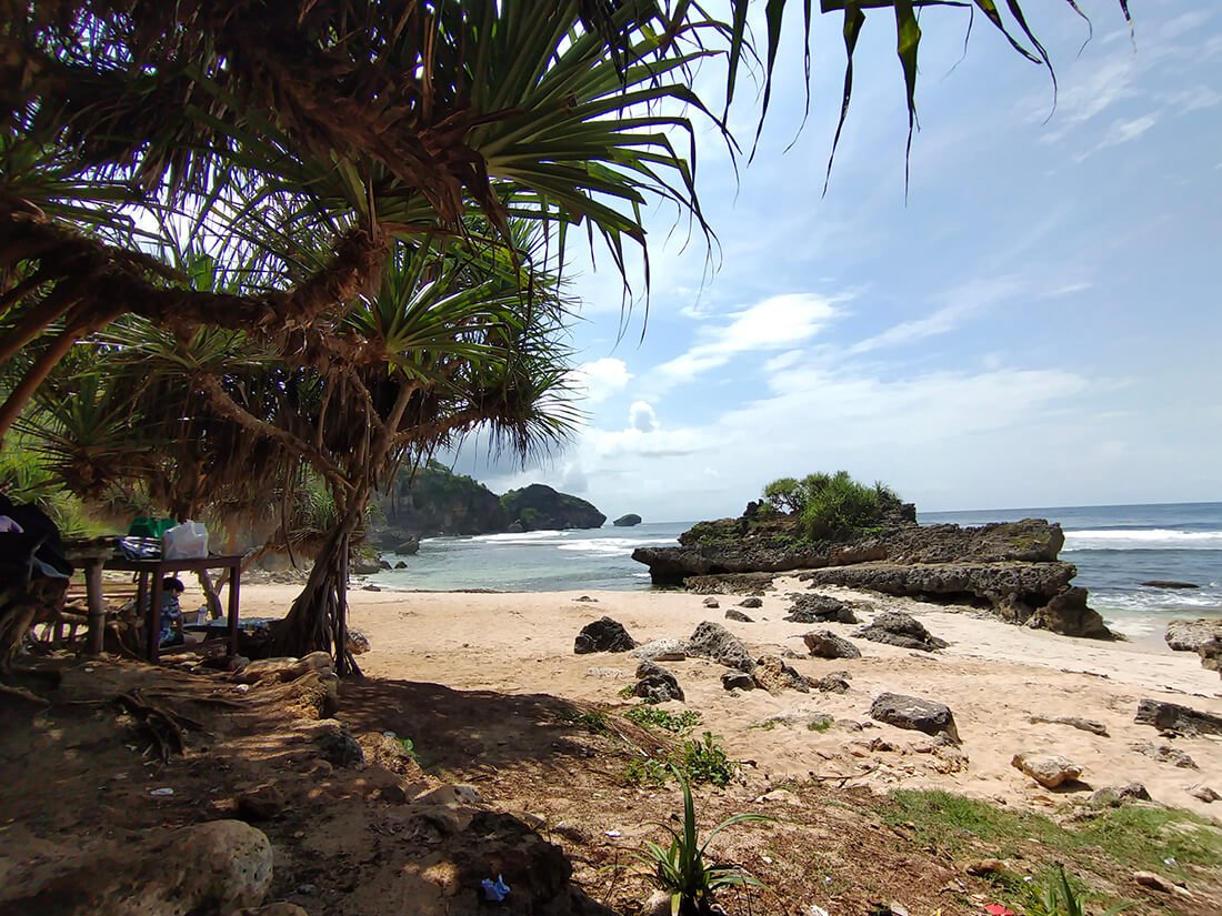 A sandy beach with rocky formations and trees providing shade at Watu Bolong Beach.