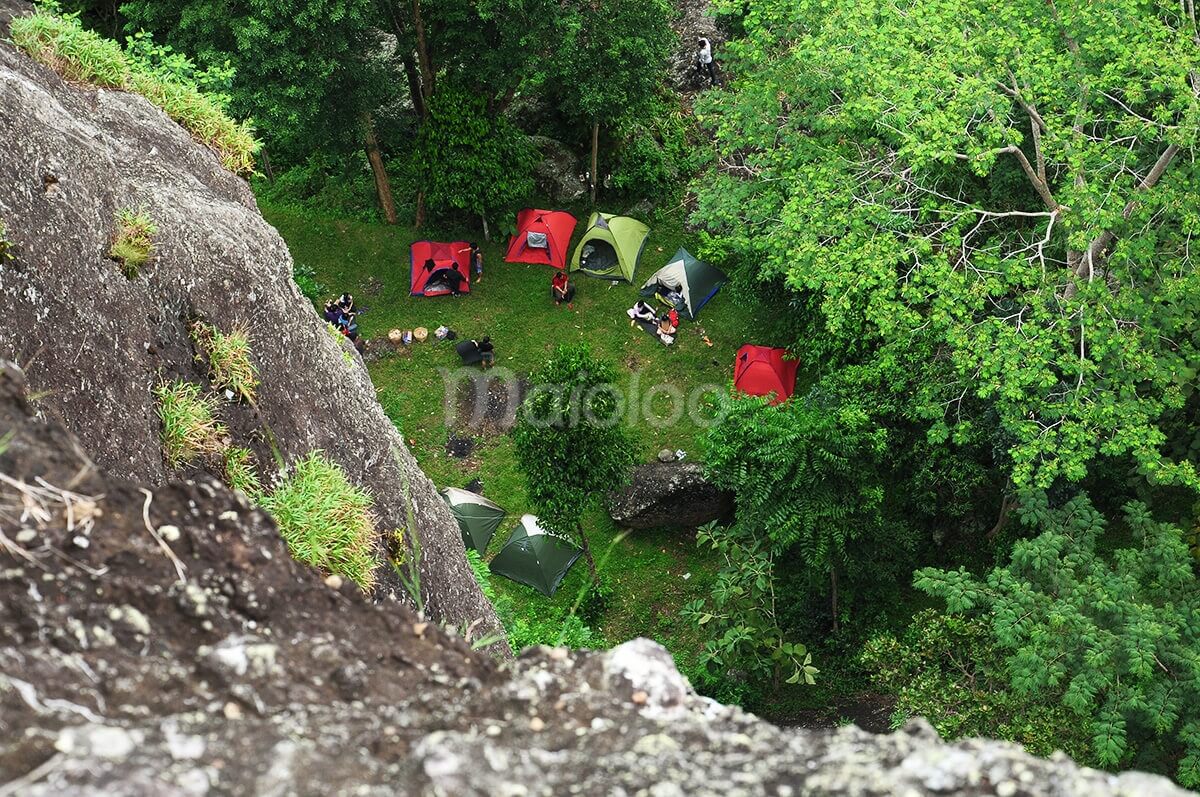 A view from above of several colorful tents set up for camping at the base of Nglanggeran Mountain.