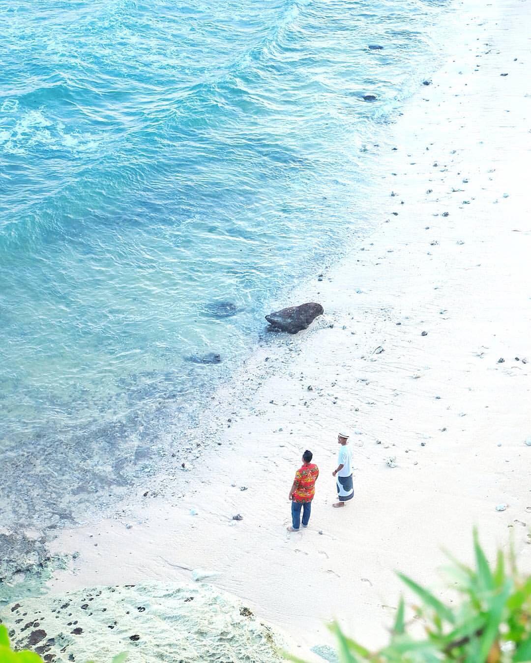 Two people walking along the edge of Sanglen Beach, near the clear blue water and white sand.