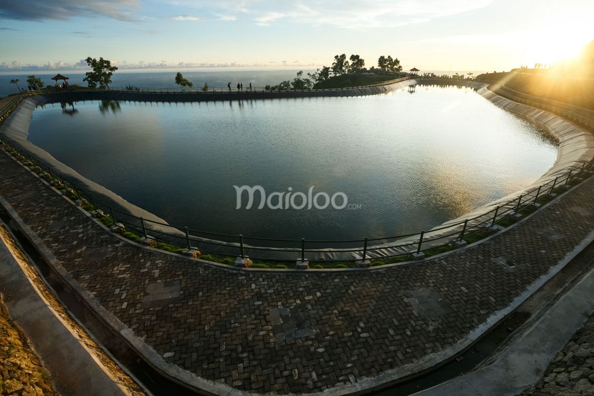 A heart-shaped reservoir enclosed with a paved path on a mountaintop during a sunny day.