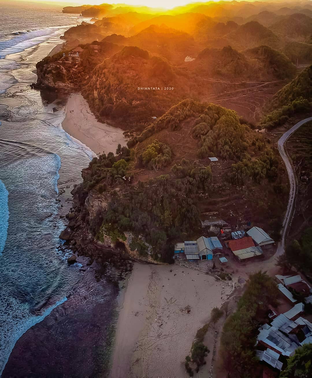 Aerial view of Watu Kodok Beach with the sun setting behind the hills.