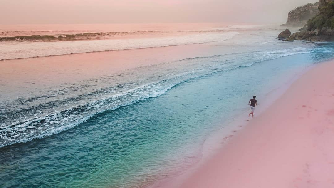 A person runs along the shore of Watu Kodok Beach during sunset.