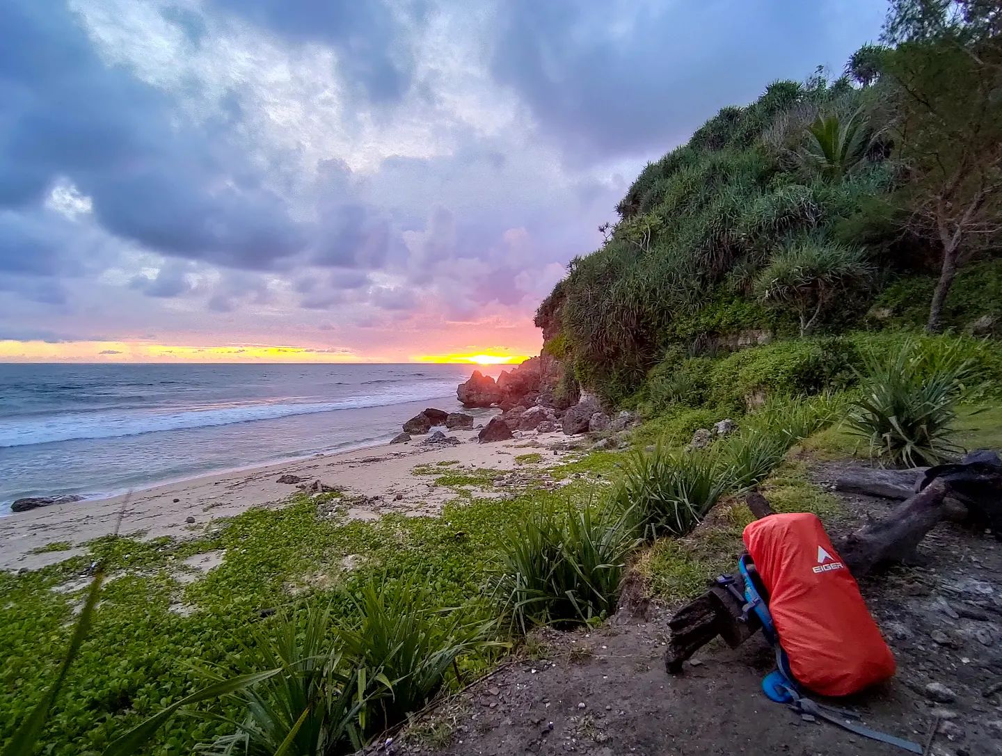 A backpack on a coastal lookout spot with a beautiful sunset over the ocean at Porok Beach.