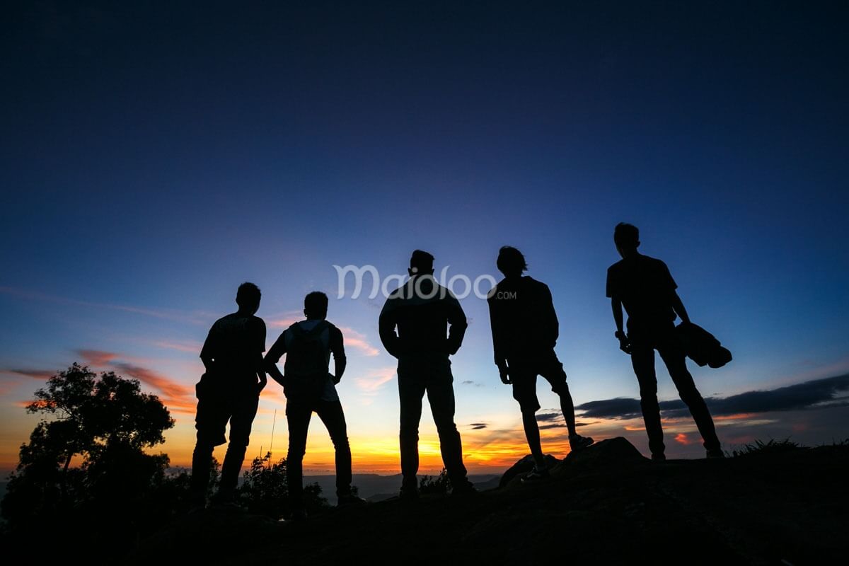 Silhouettes of five people standing on a hilltop, watching a colorful sunset.