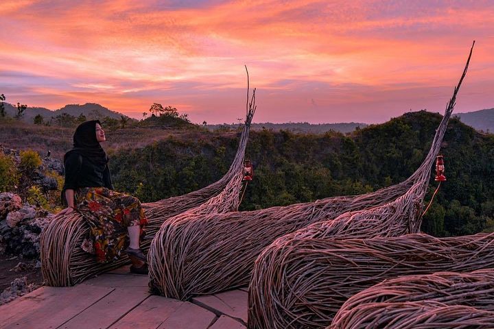 A visitor sits on unique wicker installations, enjoying the vibrant colors of the sunset sky at Geoforest Watu Payung Turunan.