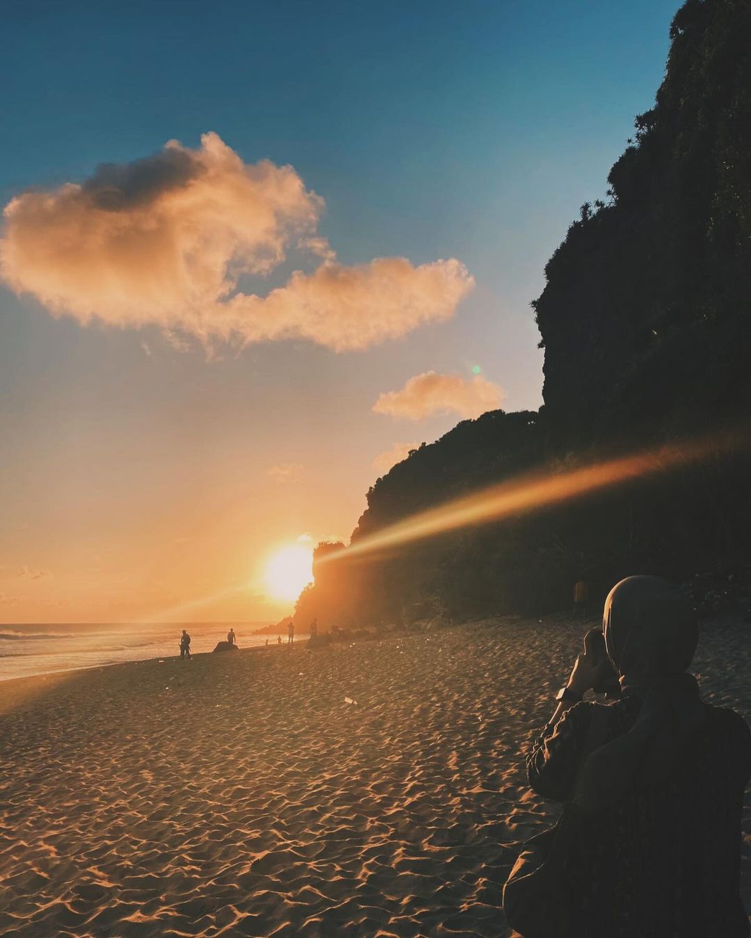 A person taking a photo of the sunset at Watunene Beach, with the sun setting behind the karst cliffs.