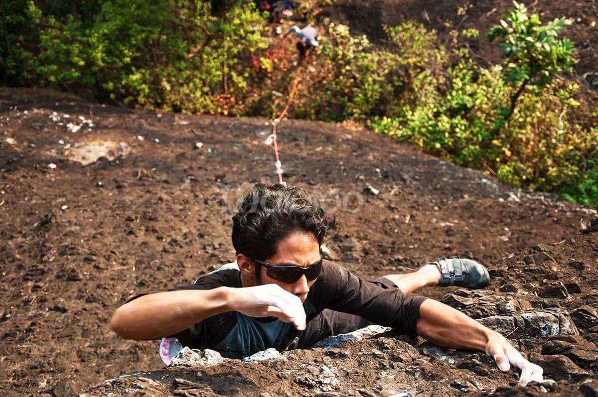 A climber gripping onto a rocky surface while rock climbing on Nglanggeran Mountain.