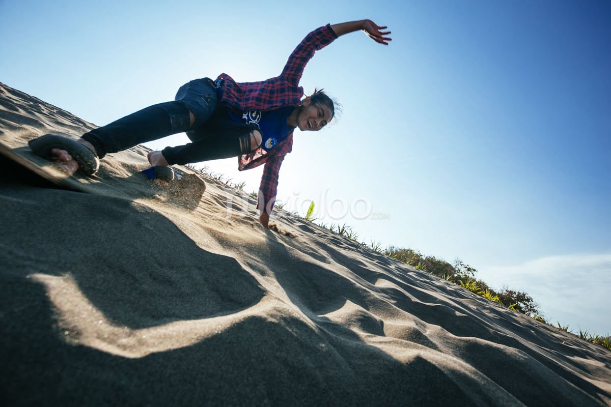 A person sandboarding down a sandy dune, balancing skillfully.