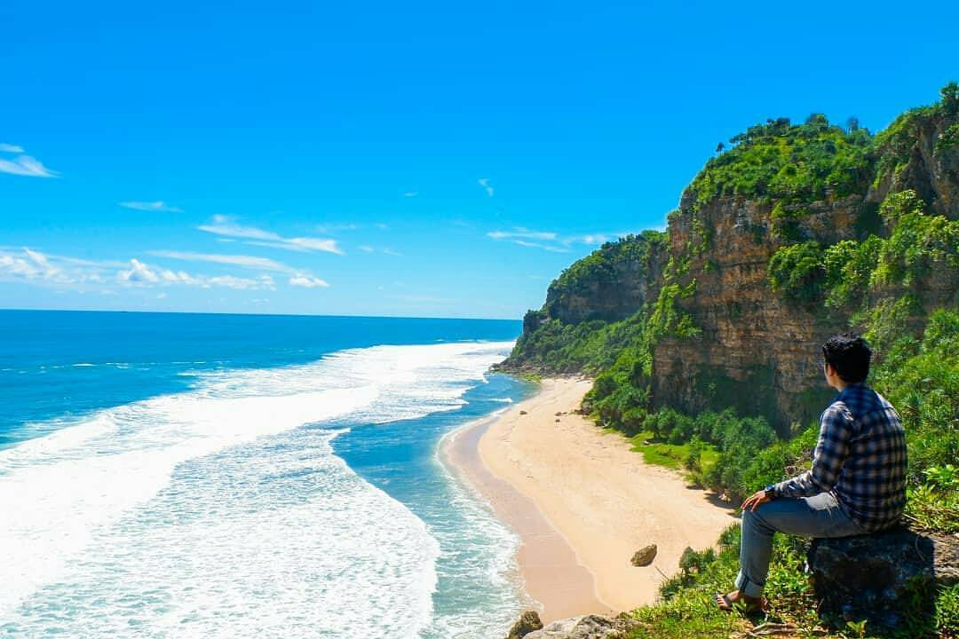 A person sitting on a rock overlooking the beautiful Watunene Beach with turquoise water and karst cliffs.