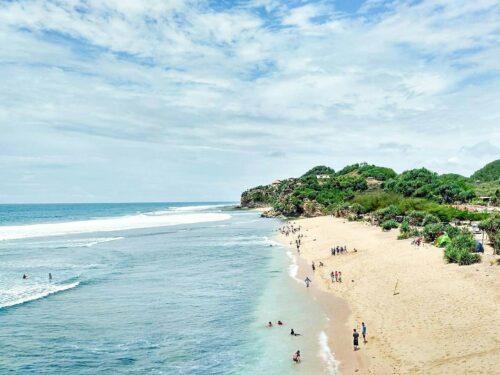 People enjoying the beach and swimming in the clear blue water at Watu Kodok Beach.