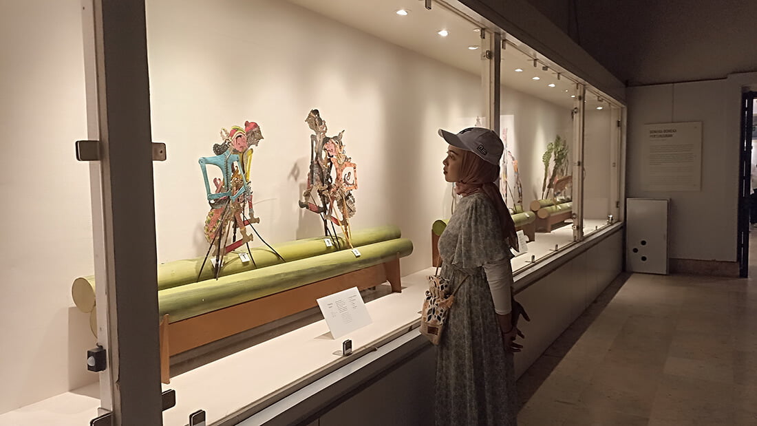 A visitor observing traditional Javanese shadow puppets (wayang kulit) displayed in a glass case at the Sonobudoyo Museum.