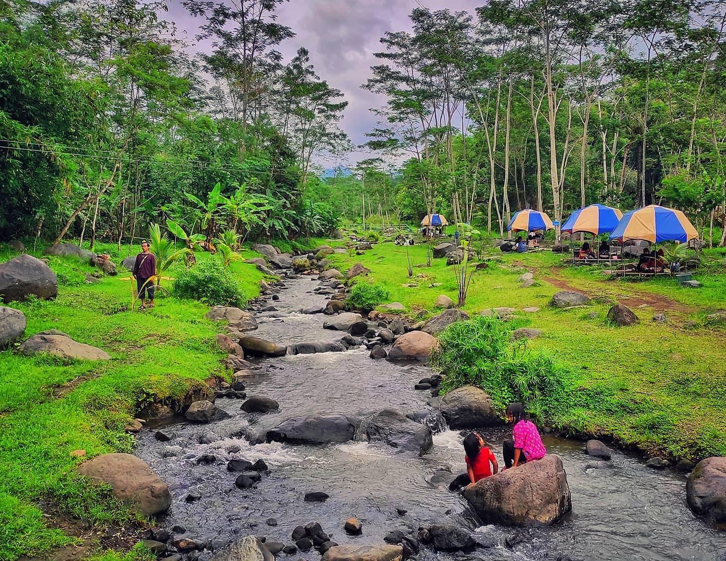 Children playing near a small river in Ledok Sambi with colorful tents in the background.