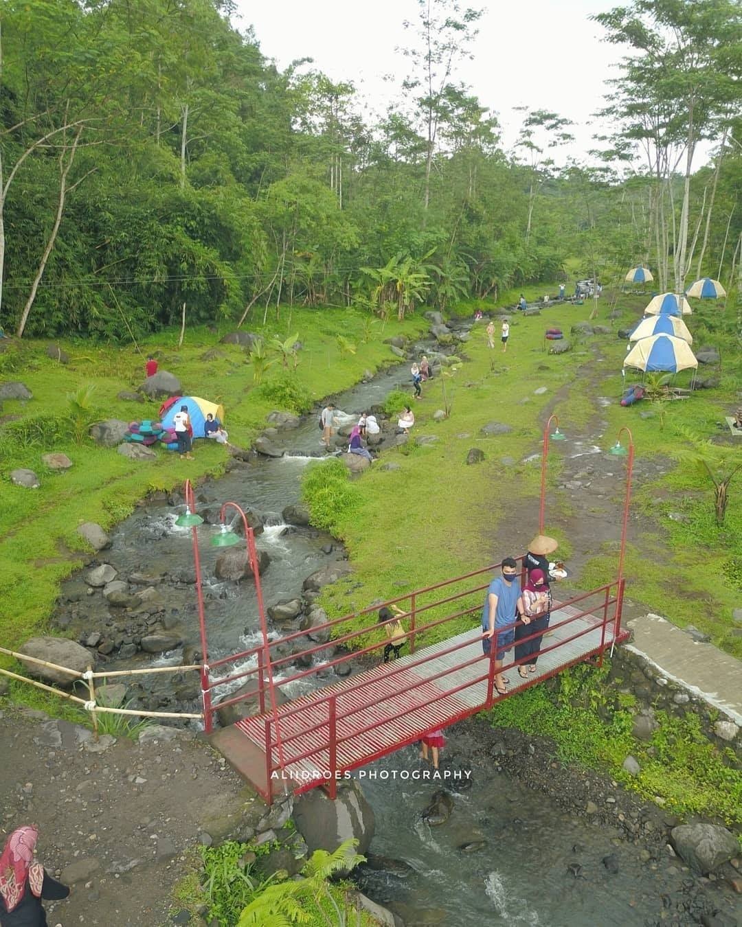 Families exploring and relaxing near a small river and a red bridge in Ledok Sambi.