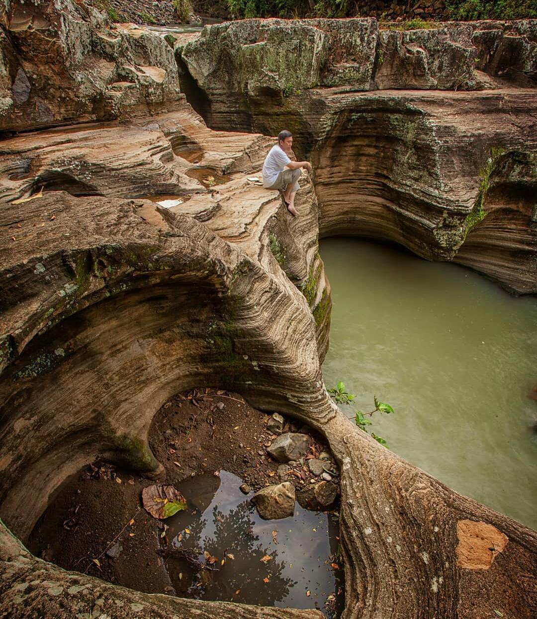 Man sitting on the edge of unique limestone formations at Luweng Sampang Waterfall in Gunungkidul, Yogyakarta, Indonesia.