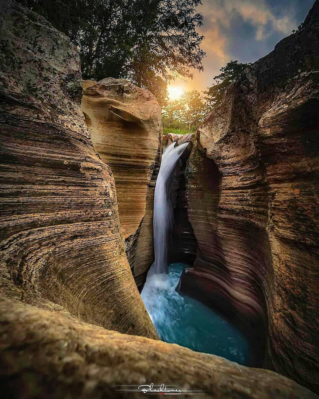 Luweng Sampang Waterfall with clear water flowing through unique limestone cliffs at sunset in Gunungkidul, Yogyakarta, Indonesia.