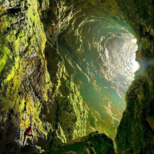 A person stands at the entrance of Ngeleng Cave, illuminated by sunlight streaming through the large vertical opening.