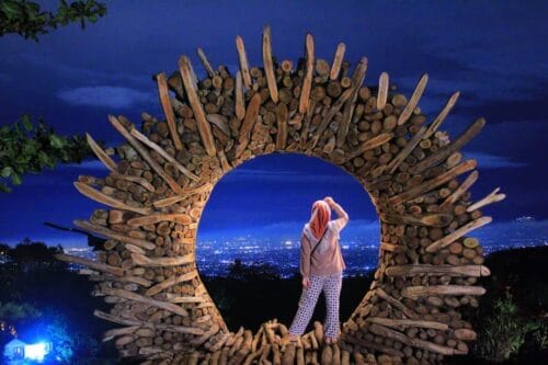 A person standing in a wooden circle structure at Mount Mungker overlooking the city lights at night.