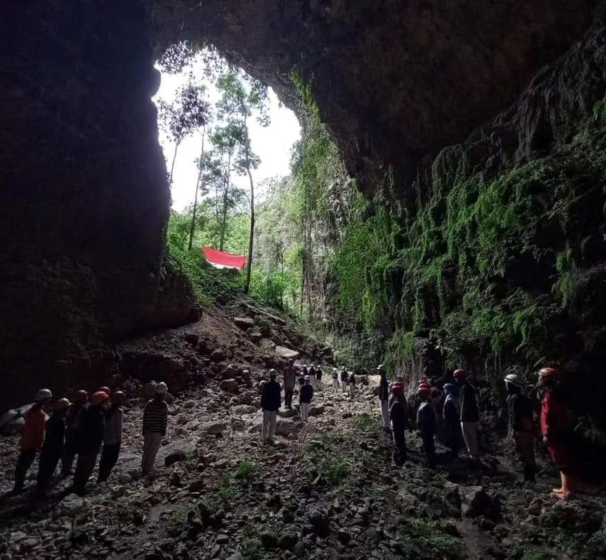 A group of people stand inside Ngeleng Cave near its entrance, with a large Indonesian flag displayed outside the cave.