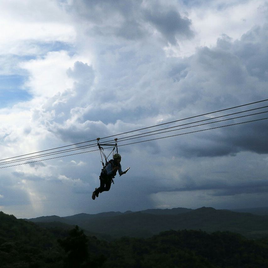 Person riding the flying fox against a backdrop of misty hills and cloudy sky at Green Village Gedangsari in Gunungkidul, Yogyakarta.