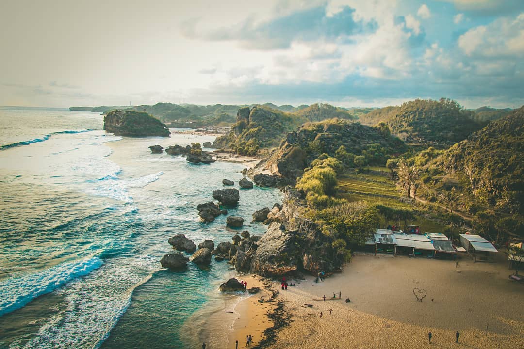 A stunning view of Ngrumput Beach with rocky cliffs and green hills taken from Kosakora Peak.