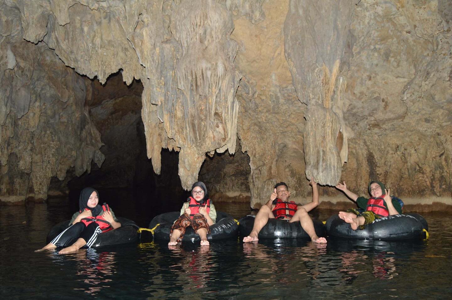 Group of visitors floating on rubber tubes inside Pindul Cave with large rock formations hanging from the cave ceiling.