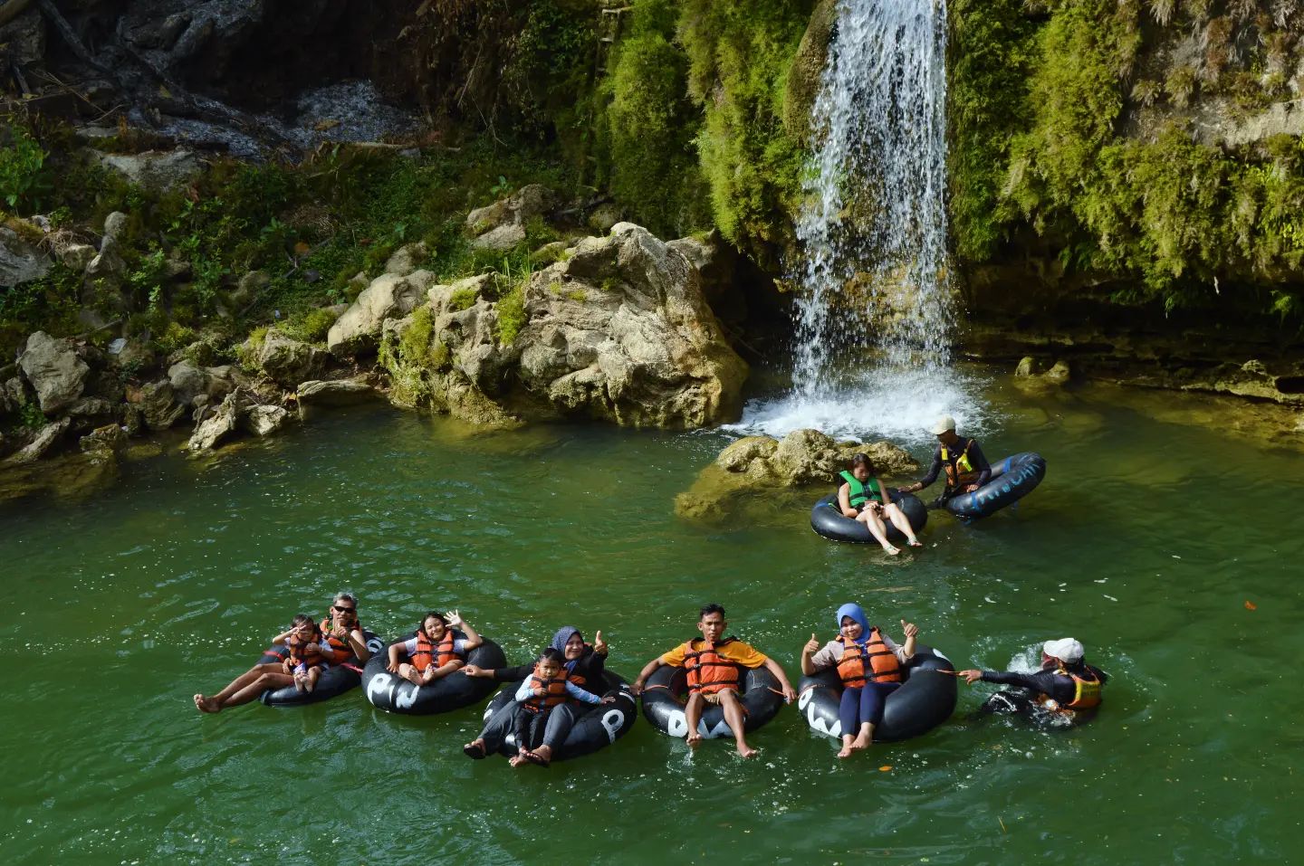 Group of visitors floating on rubber tubes in front of a waterfall at Pindul Cave.