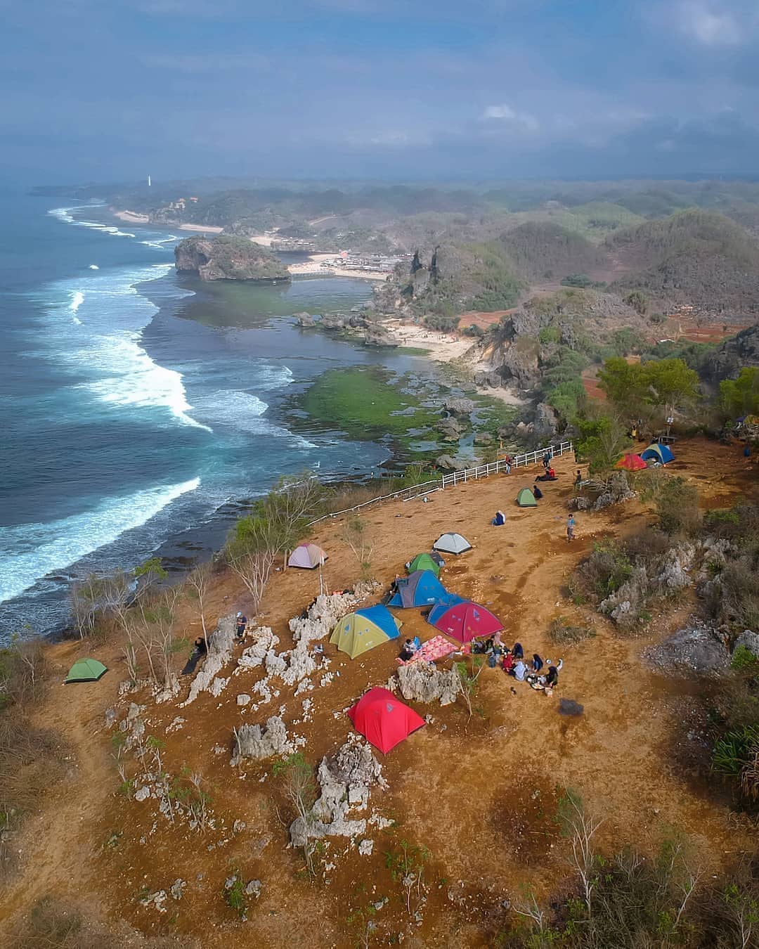 A group of colorful tents set up on Kosakora Peak overlooking the ocean and rugged coastline.