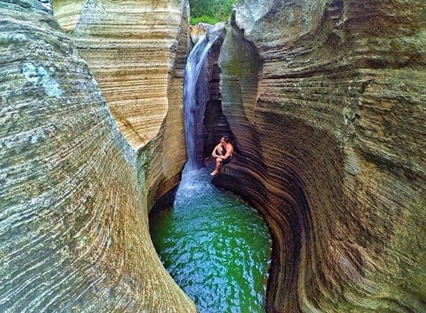 A man sitting on a rock near Luweng Sampang Waterfall with unique limestone cliffs in Gunungkidul, Yogyakarta, Indonesia.