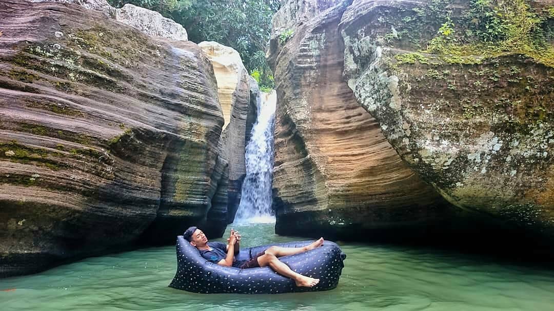 A man relaxing on an inflatable bed in the water near Luweng Sampang Waterfall with unique limestone cliffs in Gunungkidul, Yogyakarta, Indonesia.