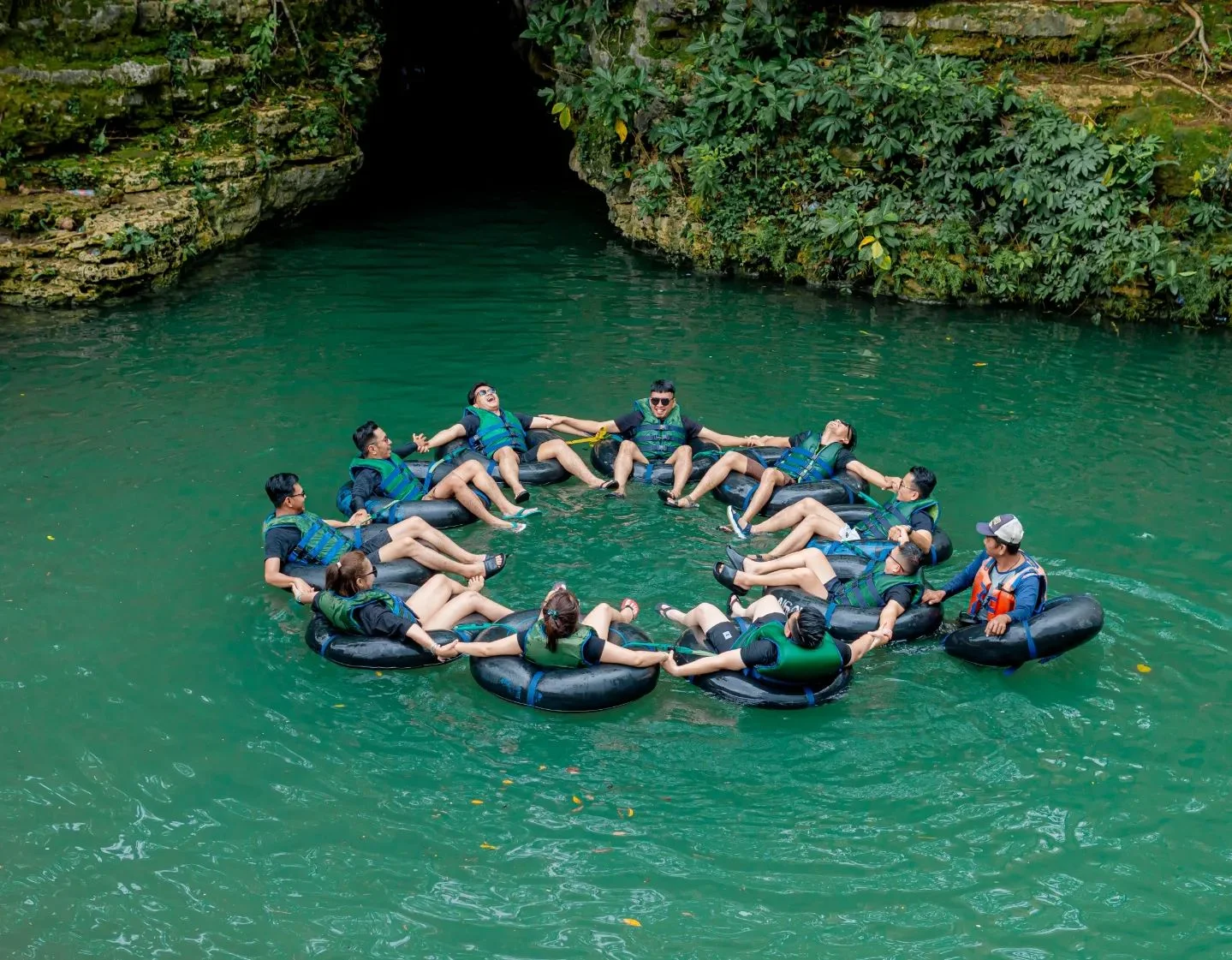 Group of visitors forming a circle while floating on rubber tubes in the emerald waters near Pindul Cave.