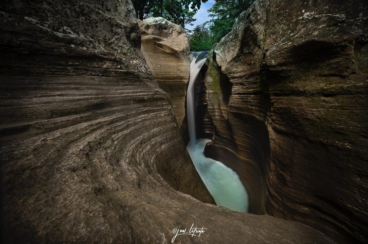 Luweng Sampang Waterfall flowing through narrow limestone cliffs with intricate patterns in Gunungkidul, Yogyakarta, Indonesia.