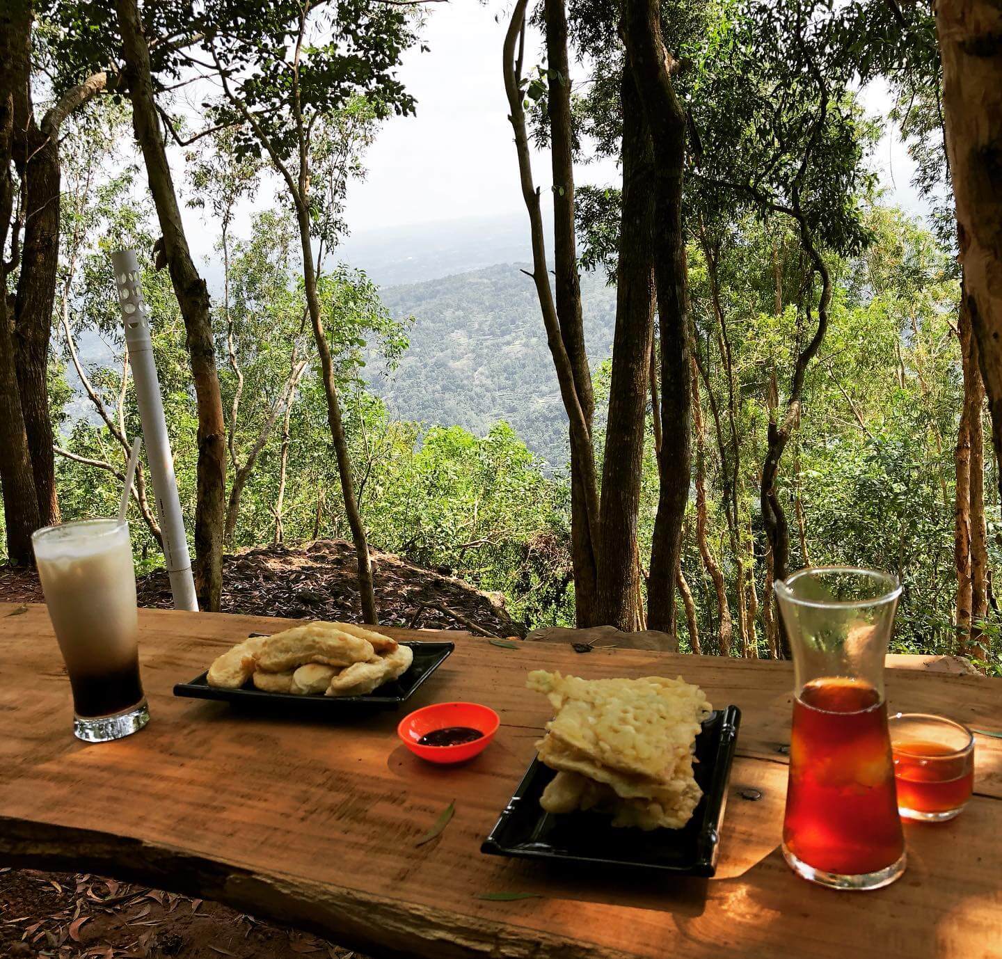 Table with drinks and snacks overlooking a lush green forest at Hutan Pinus Pengger.