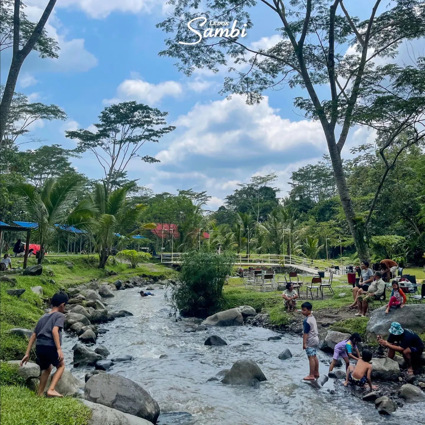 Children and families playing and relaxing by a small river in Ledok Sambi under a blue sky.