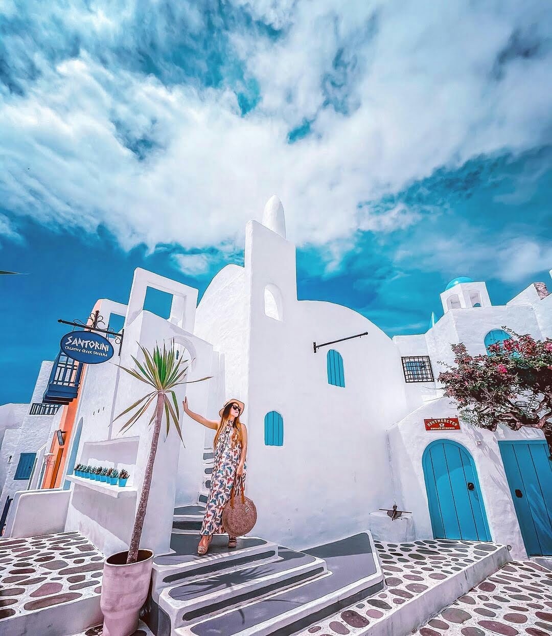 A visitor posing in front of white buildings with blue doors and windows resembling Santorini at Bhumi Merapi Agrotourism.