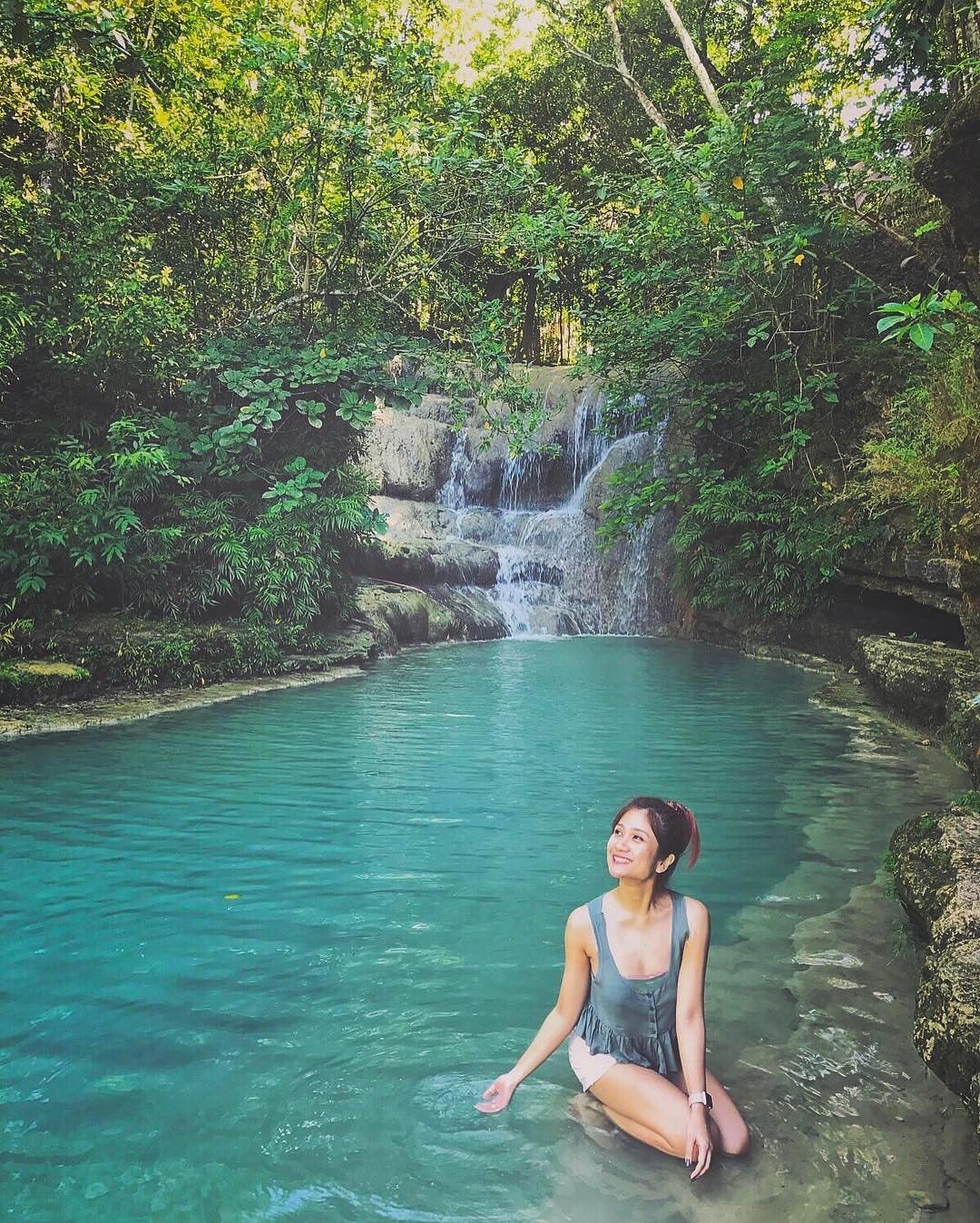 A woman enjoying the turquoise pool at Lepo Waterfall, with cascading water and lush greenery around in Yogyakarta.