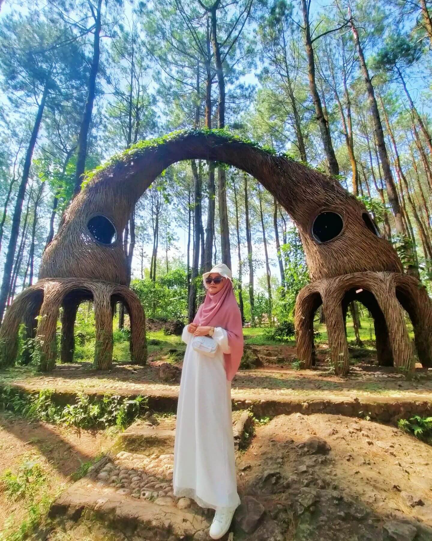 Woman standing in front of a woven art installation in the pine forest at Hutan Pinus Pengger.