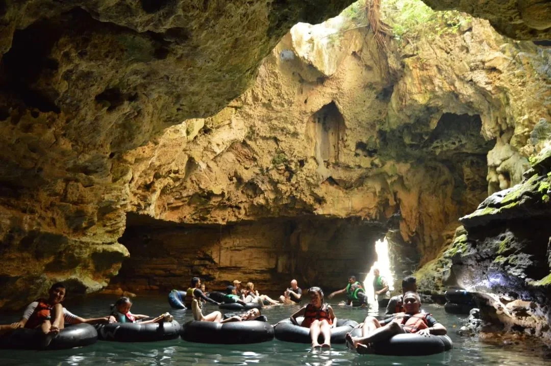 Visitors floating on rubber tubes in the emerald waters of Pindul Cave, surrounded by illuminated rock formations.