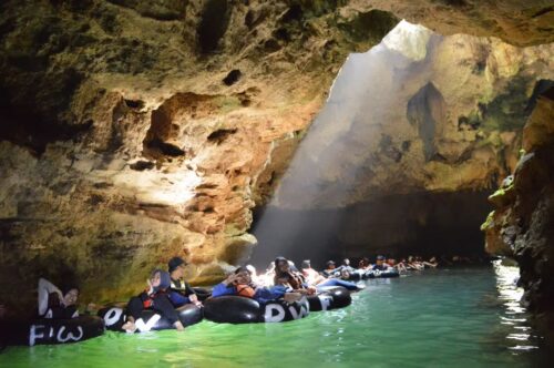 Visitors floating on rubber tubes through the emerald waters of Pindul Cave with sunlight streaming through the cave opening.