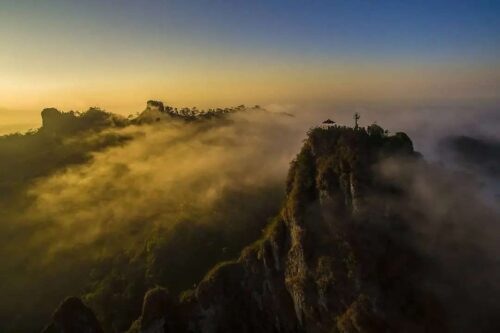 A breathtaking sunrise view above the clouds from Suroloyo Peak in Yogyakarta, Indonesia, with the Menoreh Hills bathed in morning light and mist.